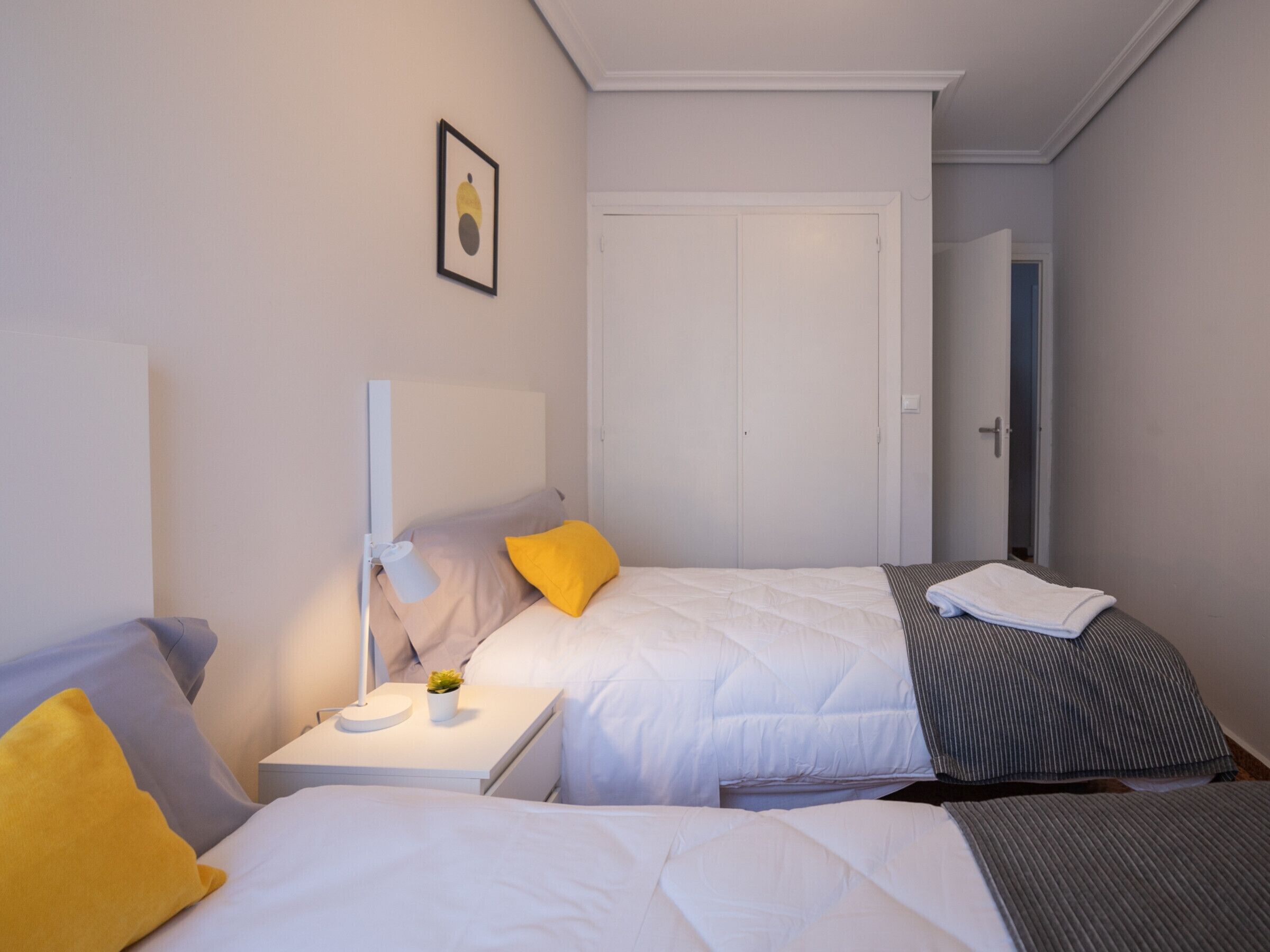 Ein Hotelzimmer mit zwei Betten, einem Nachttisch mit Lampe und einer Tür zu einem weiteren Raum.