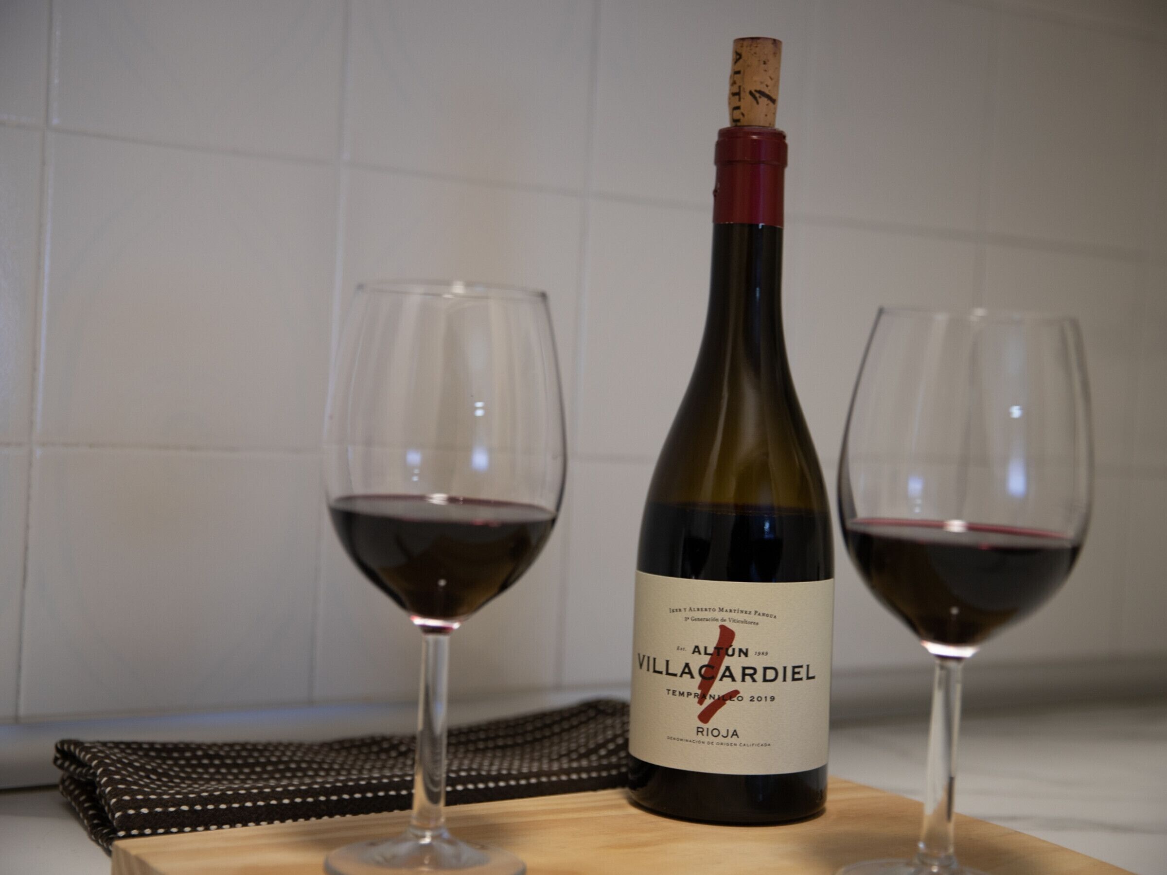 Una botella de vino Villacardiel con dos copas de vino tinto sobre una tabla de madera.