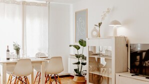 Un salon moderne avec un coin repas, doté d’un parquet, de meubles blancs, d’un téléviseur et d’une plante en pot.