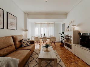 En moderne stue med en brun lædersofa, et træsofabord og et spiseområde med et hvidt bord og stole.