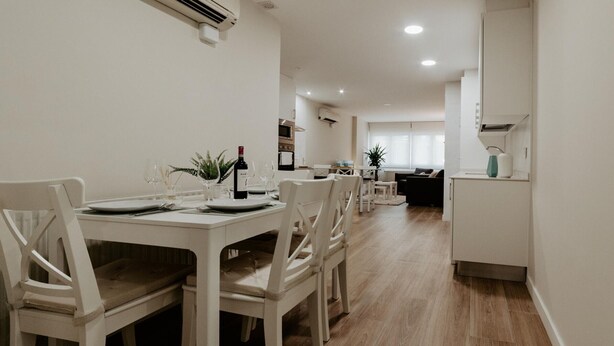 A dining area with a white table set for four, a kitchen in the background, and a living area with a sofa and a plant. - Charming apartment in Logroño for 4, includes Wi-Fi (Logroño)