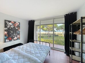 Un dormitorio con cama, un ventanal con vistas a árboles y una playa, y una cortina negra.