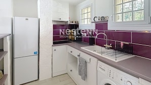 A compact kitchen with white cabinets, a built-in dishwasher, and a window with a view.