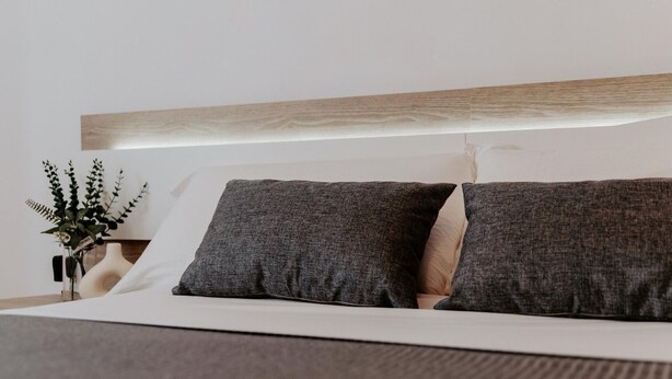 A neatly made bed with a wooden headboard, two grey pillows, and a beige pillow. - Comfortable Apartment with Terrace in Logroño (Logroño)