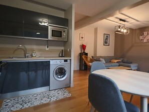 A compact living space with a kitchen area, a washing machine, a dining table, and a seating area with a sofa and chairs. - Comfort 4* with Parking and Terrace at Mont-Dore (Mont-Dore)