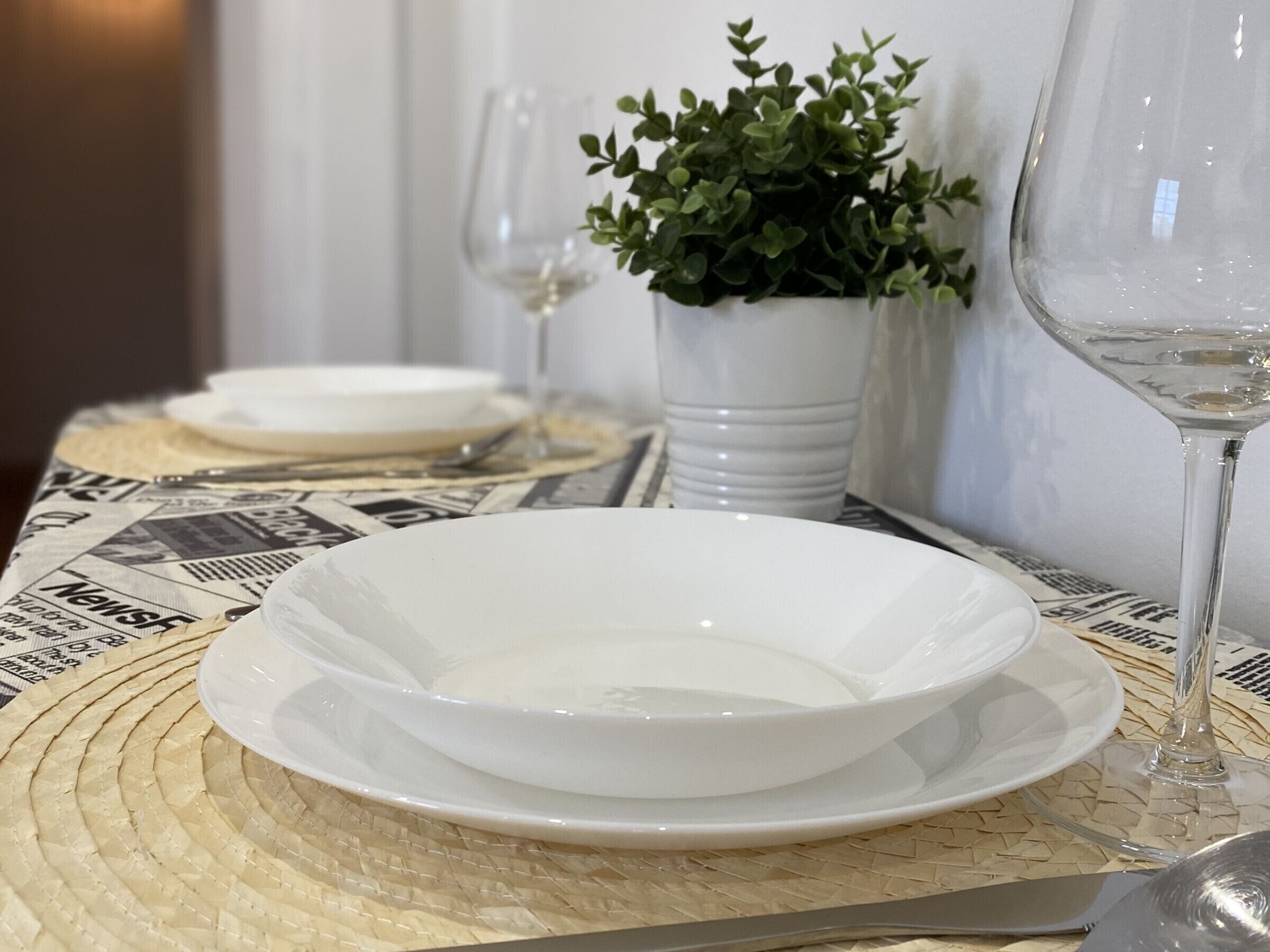 Een eettafel met witte borden, een glas witte wijn en een kleine plant in een pot.