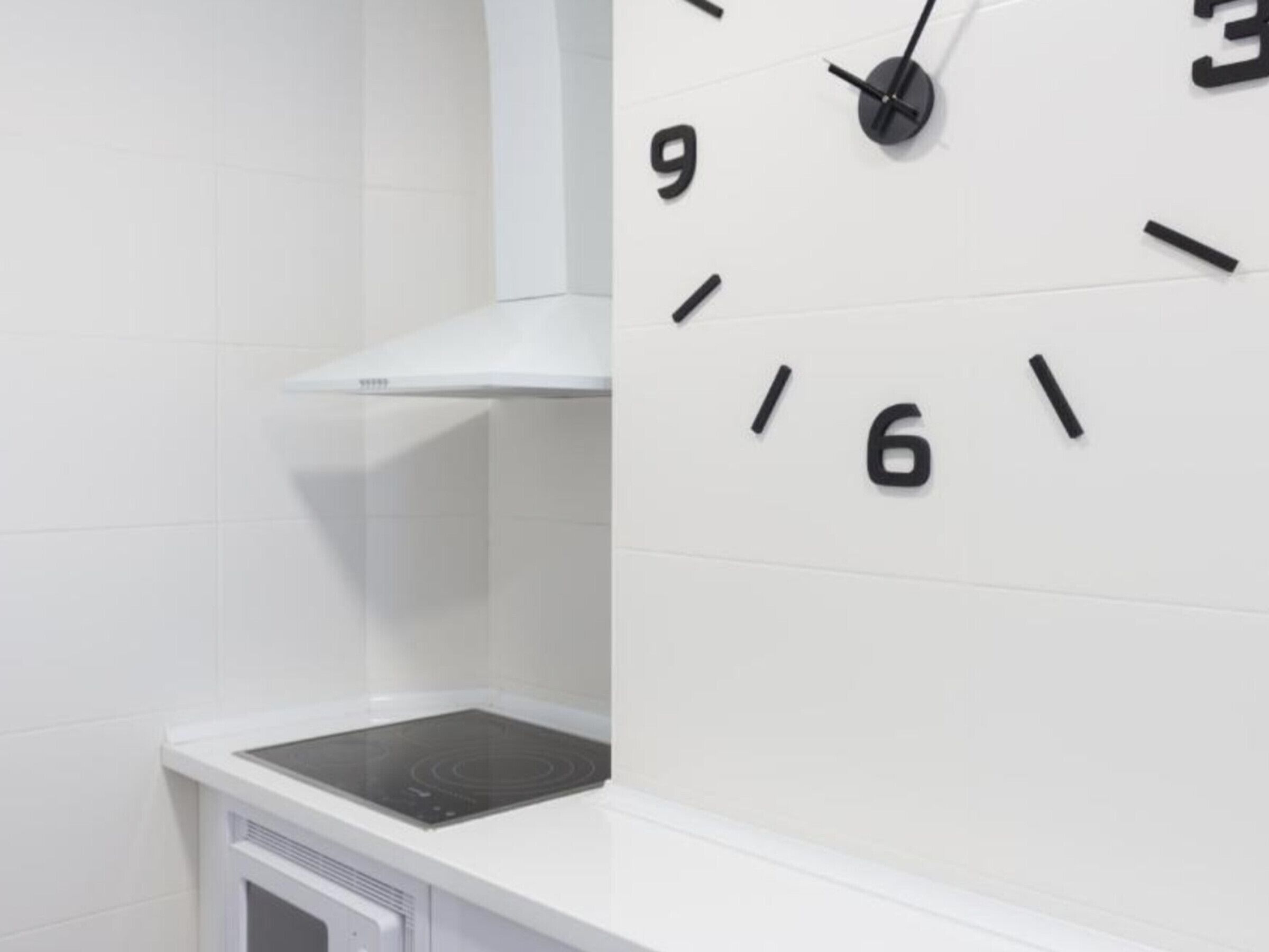 A kitchen with white tiles, a stove, and a wall clock.