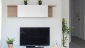 A modern living room with a flat-screen TV on a white console, a small potted plant, and a white lantern on the console. - Renovated Apartment in Central Logroño with Private Parking (Logroño)