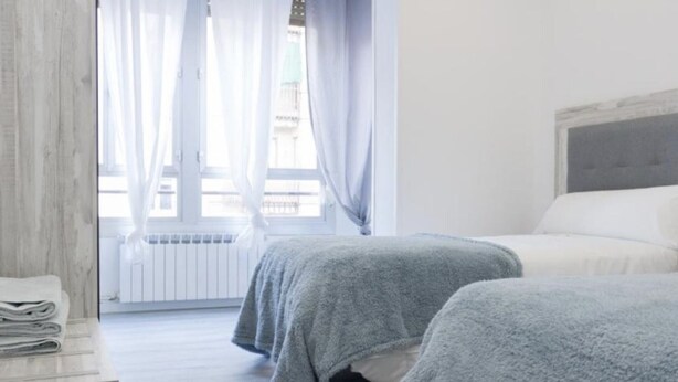 A hotel room with two beds, a wooden dresser, and a window with sheer curtains. - Renovated Apartment in Central Logroño with Private Parking (Logroño)