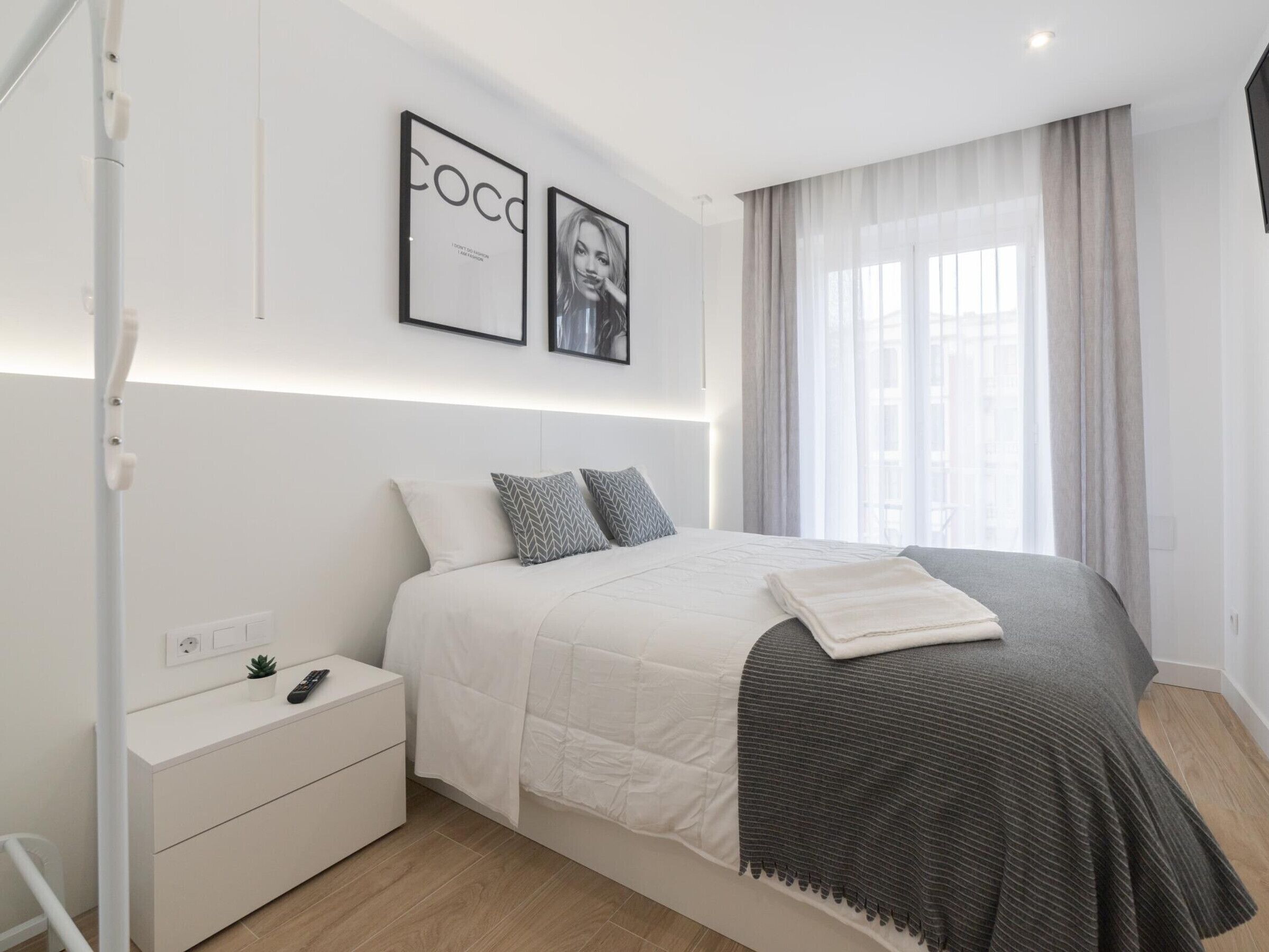 Une chambre à coucher moderne avec un lit, des tables de chevet, une petite table d’appoint, une petite plante et des tableaux encadrés accrochés au mur.