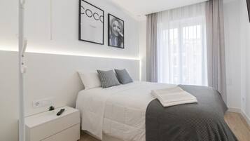 Une chambre à coucher moderne avec un lit, des tables de chevet, une petite table d’appoint, une petite plante et des tableaux encadrés accrochés au mur.