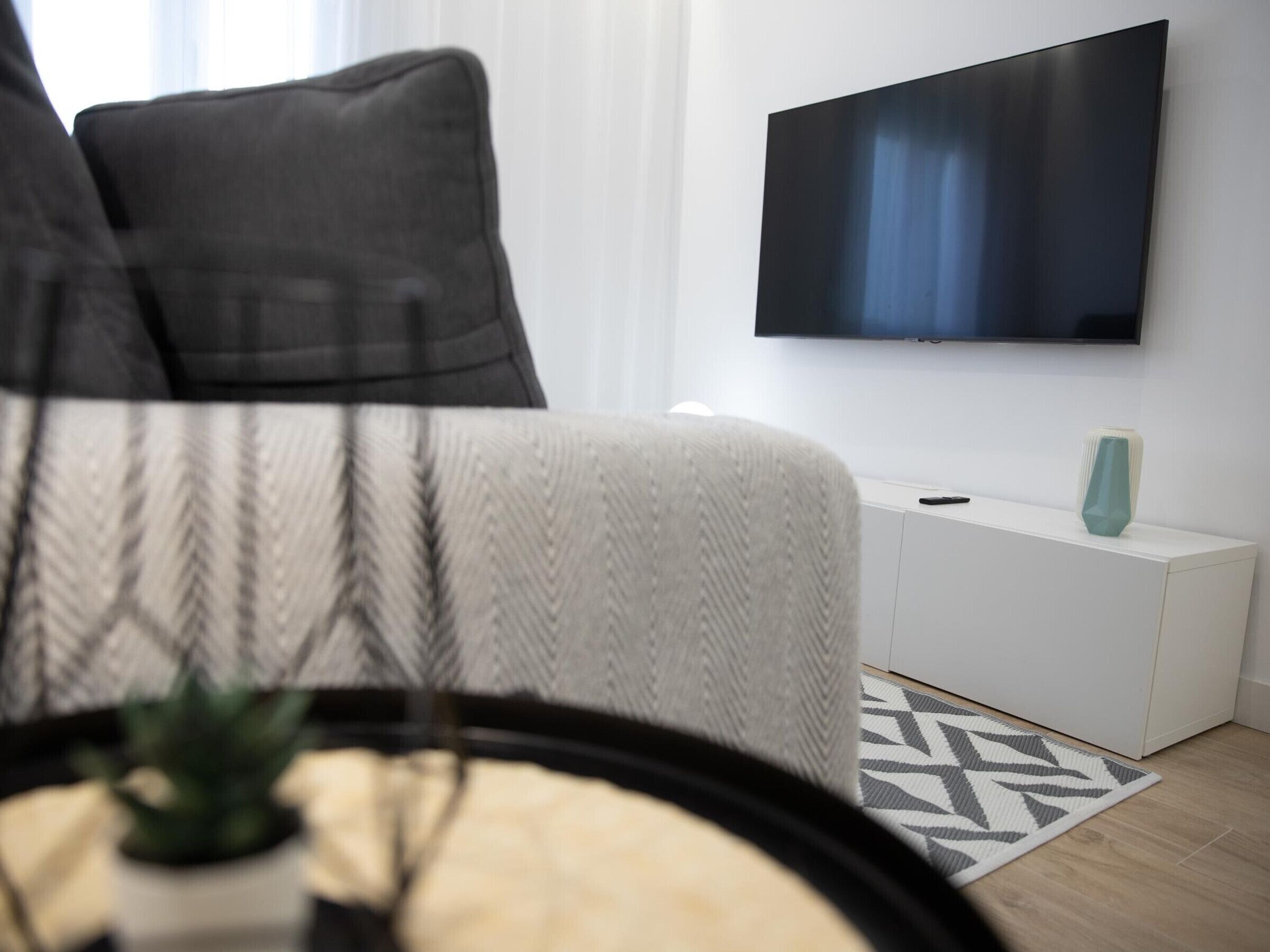 Ett modernt vardagsrum med en soffa, en tv som är monterad på väggen, ett litet vitt sidobord och en mönstrad matta.