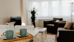 A modern living room with a white table, two teal cups, and a white pitcher on a woven tray. A dark sofa and a small white side table are in the background. - Central Renovated Apartment with Wi-Fi in Logroño (Logroño)