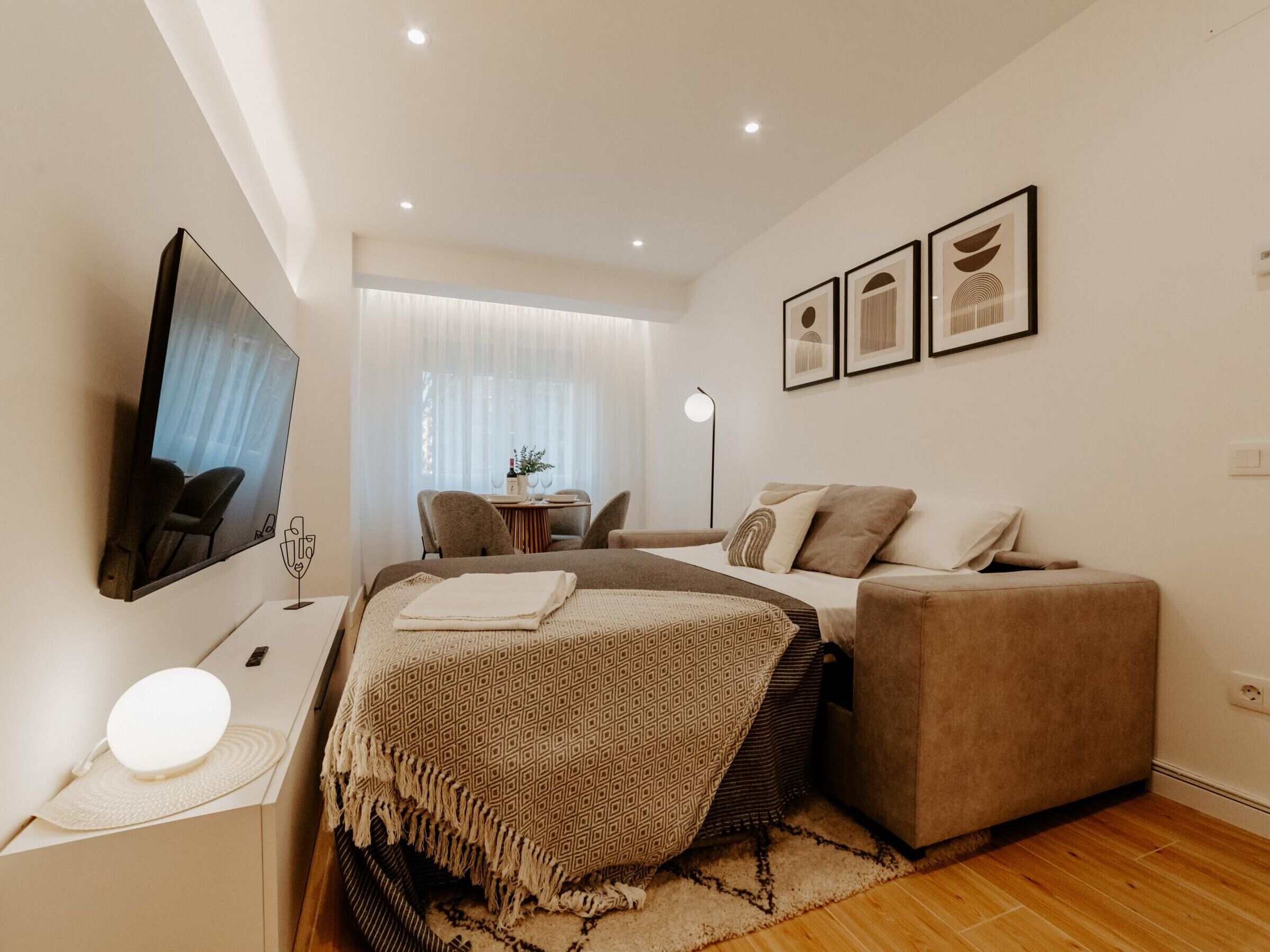 A modern bedroom with a bed, a sofa, a TV, and a small table with a lamp.