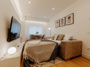 Un dormitorio moderno con cama, sofá, televisión y una pequeña mesa con lámpara.