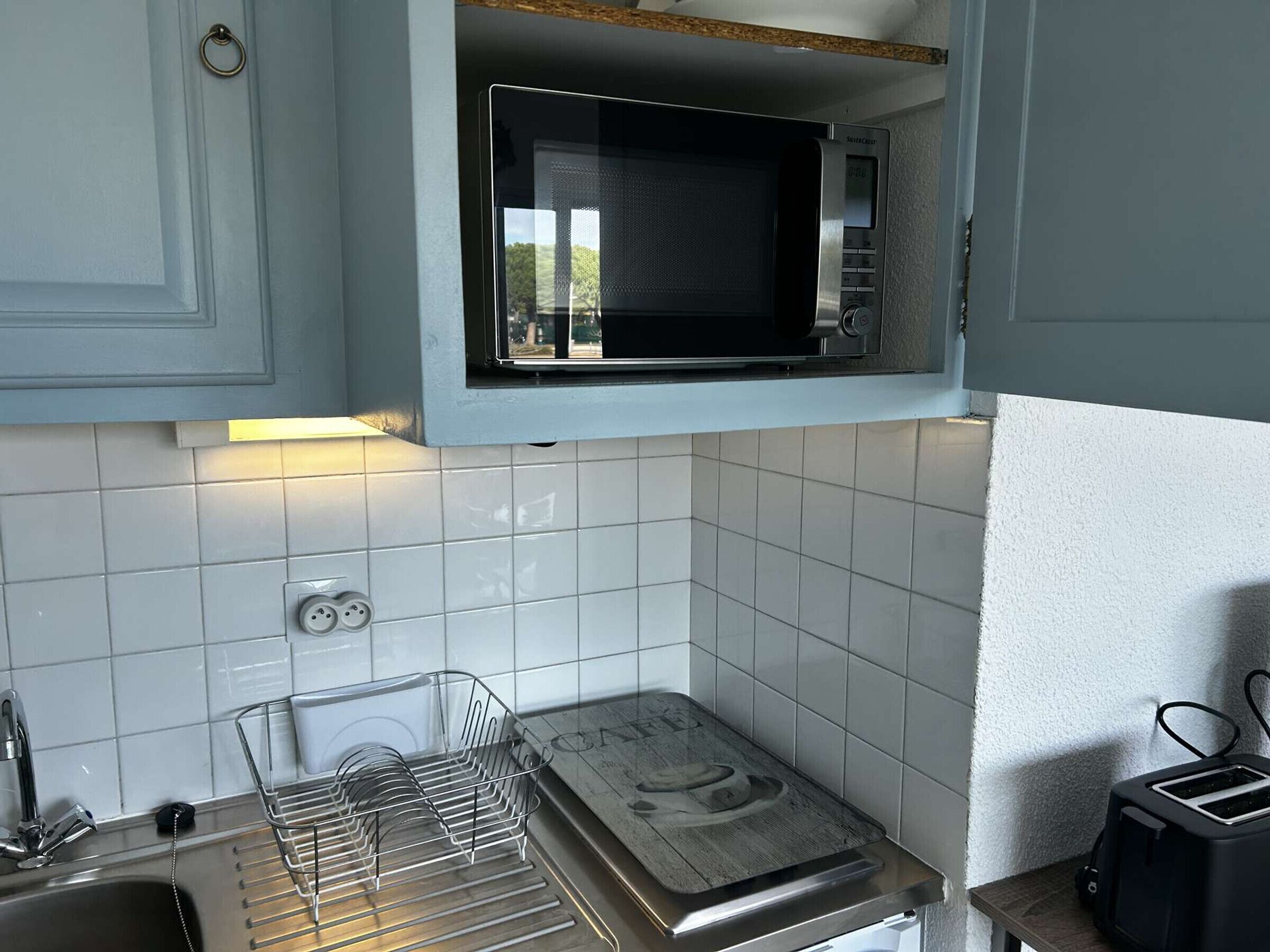 A compact kitchen with a microwave, a toaster, and a dish rack.