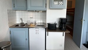 Una cocina compacta con armarios azul claro, un refrigerador blanco, un tostador y una cafetera.