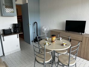 A compact living space with a kitchenette, a dining area with four chairs, a coffee maker, a fan, and a television. - Studio cabin for 4 in Port Camargue with terrace and private parking (Port Camargue)