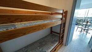 Un banco de madera con cojines estampados en una habitación con suelo de baldosas y vistas a un espacio exterior con sillas y una mesa.