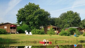 A lakeside cabin area with wooden cabins, a small dock, and a reflection in the water. - Mobile Home with Terrace for 6 persons (Sainte-Reine-de-Bretagne)
