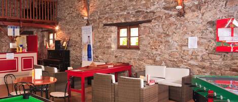 Un ambiente acogedor en el interior con mesa de billar, mobiliario de mimbre y mesa de futbolín.