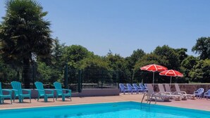 A swimming pool with blue water, surrounded by turquoise and white lounge chairs and red umbrellas. - Mobile Home with Terrace for 6 persons (Sainte-Reine-de-Bretagne)