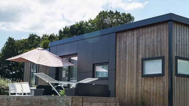 A modern cabin with a wooden exterior, a patio area with outdoor furniture, and a staircase leading to the entrance. - Mobile Home with Terrace for 6 persons (Sainte-Reine-de-Bretagne)