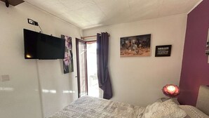 Ein Schlafzimmer mit einem Bett, einem Flachbildfernseher an der Wand, einem Fenster mit Vorhängen und einer Wandlampe.