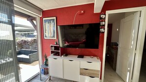 Ein Wohnzimmer mit roter Wand, einem Flachbildfernseher, einer weißen Unterhaltungseinheit und einer Glastür zum Balkon.