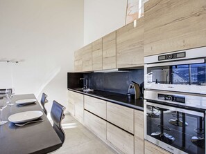 Eine moderne Küche mit Essbereich, ausgestattet mit einer schwarzen Arbeitsplatte, Edelstahlgeräten und hellen Holzschränken.