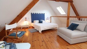 Um quarto de sótão aconchegante, com teto inclinado, uma cama, um sofá, uma cadeira e uma mesinha.