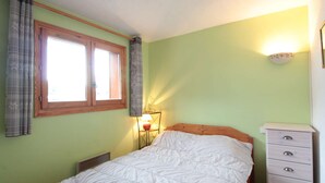 Een slaapkamer met een bed, een dressoir, een raam met gordijnen en een wandlamp.