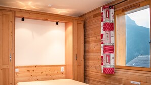 Een houten kamer met een bed, een raam met uitzicht op bergen, en een quilt aan de wand.