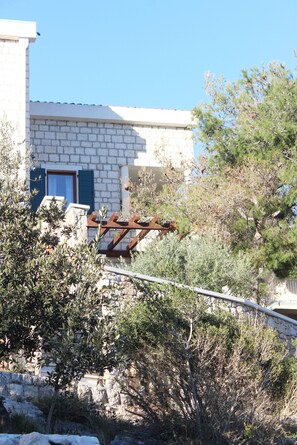 Un bâtiment en pierre avec une porte et des volets bleus, entouré de végétation et d’une structure métallique.