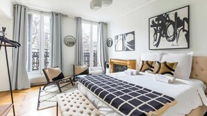 A modern bedroom with a large bed, a fireplace, and artwork on the walls. - Elegant 3BR Bastille Apartment (Paris)