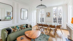 A living room with a green sofa, wooden coffee table, and a dining area with a glass table and chairs. - Elegant 3BR Bastille Apartment (Paris)