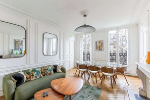 A living room with a green sofa, wooden coffee table, and a dining area with a glass table and chairs. - Elegant 3BR Bastille Apartment (Paris)