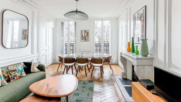 A spacious living room with a dining area, large windows, a fireplace, and a television. - Elegant 3BR Bastille Apartment (Paris)