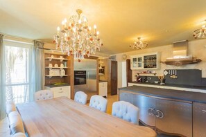 A modern kitchen with a wooden dining table, white chairs, and a chandelier. - Luxury Villa in Tremezzo (Tremezzo)