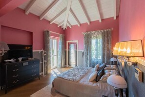 A bedroom with a pink wall, a bed with a patterned bedspread, a dresser, a television, and a lamp. - Luxury Villa in Tremezzo (Tremezzo)