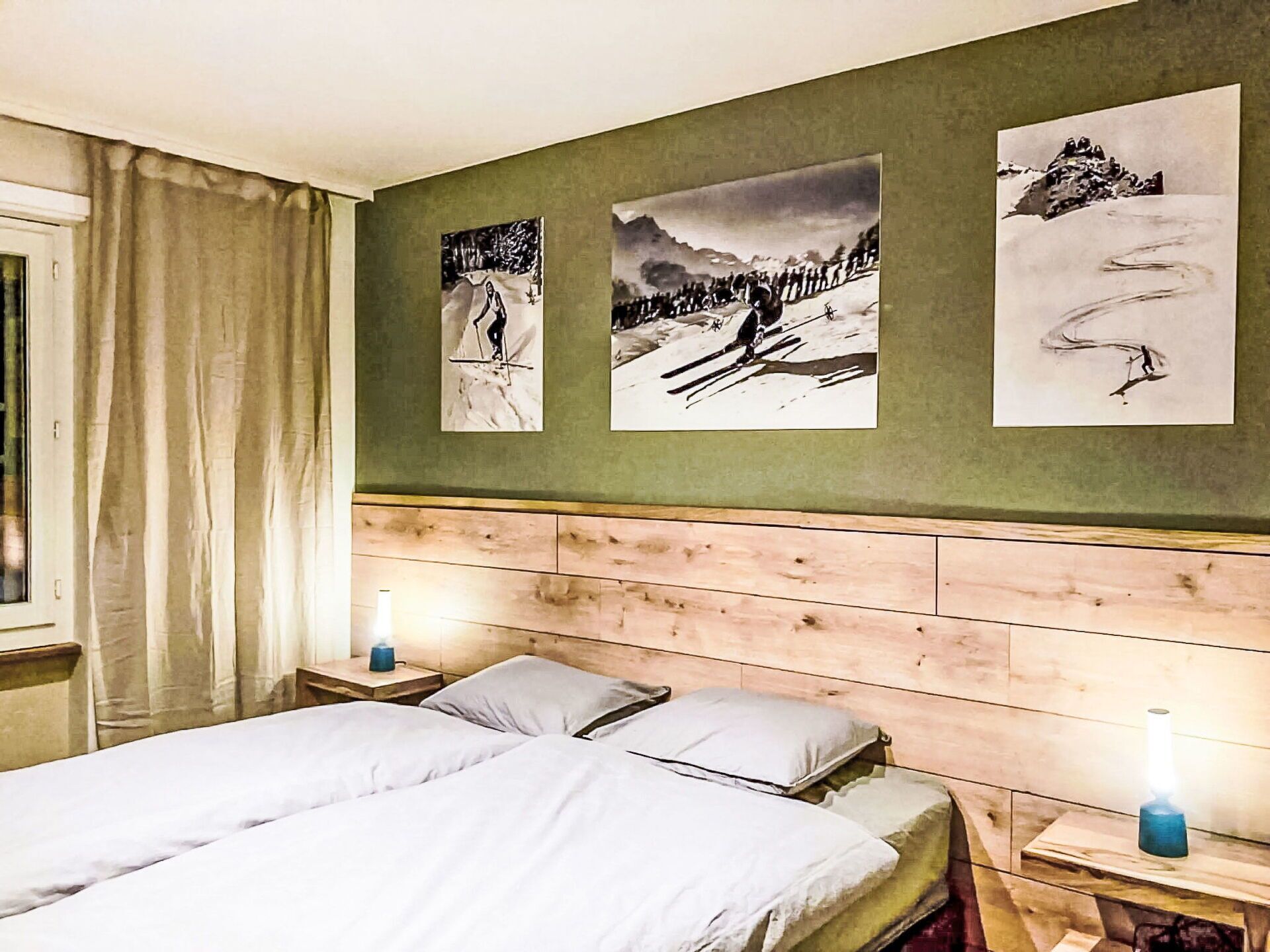 A bedroom with a wooden headboard, two bedside tables with lamps, a bed with white bedding, and three framed pictures on the wall.
