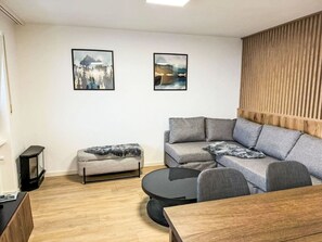 A modern living room with a grey sectional sofa, a small ottoman, a round coffee table, and two framed landscape paintings on the wall. - Beautiful apartment for 4 people with WIFI, TV and balcony (Leukerbad)