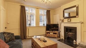 Ein Wohnzimmer mit einer Couch, einem Couchtisch, einem Fernseher, einem Kamin und einem großen Fenster mit Vorhängen.