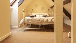 Ein Schlafzimmer mit schrägverdeckter Decke, einem Bett mit weißem Metallgestell, einer herzförmigen Wanddekoration und einem Fenster.