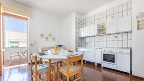 A compact kitchen with white cabinets, a built-in oven, and a dining area with a round table and chairs. - Nice apartment for 8 guests with TV and balcony, close to Gallipoli (Baia Verde)