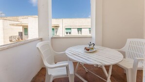 A balcony with a round table and two white plastic chairs, a small tray with cups and a pot, and a view of buildings with green shutters. - Nice apartment for 8 guests with TV and balcony, close to Gallipoli (Baia Verde)