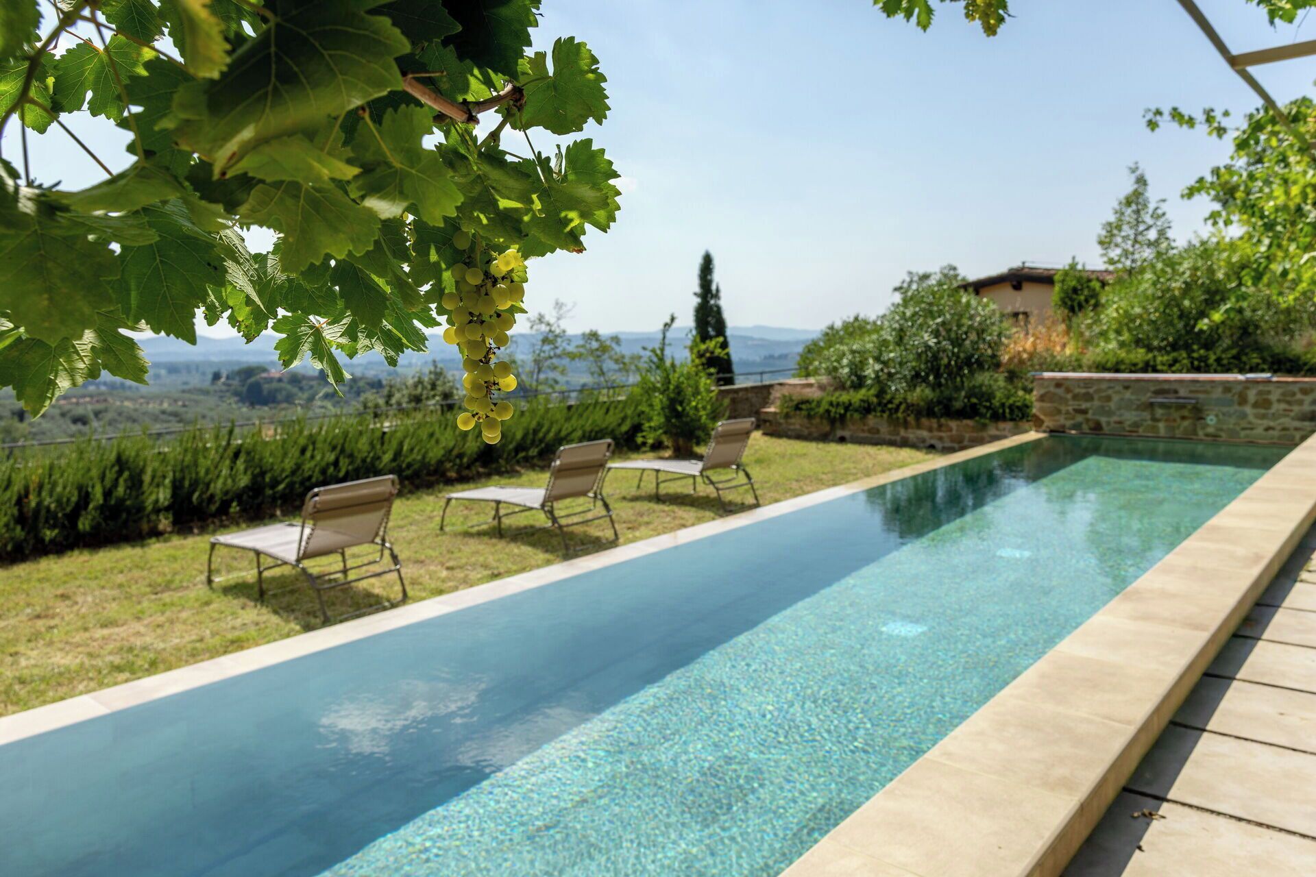 A swimming pool with clear water, surrounded by grass and a stone wall.