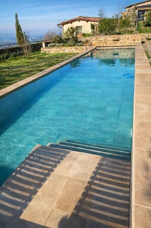 Ein rechteckiger Swimmingpool mit klarem, blauem Wasser, umgeben von einer Steinmauer und einer gefliesten Liegefläche.