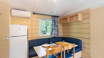 Une petite cuisine équipée comprenant un réfrigérateur, une fenêtre avec des rideaux, une table à manger avec des chaises et un banc intégré.