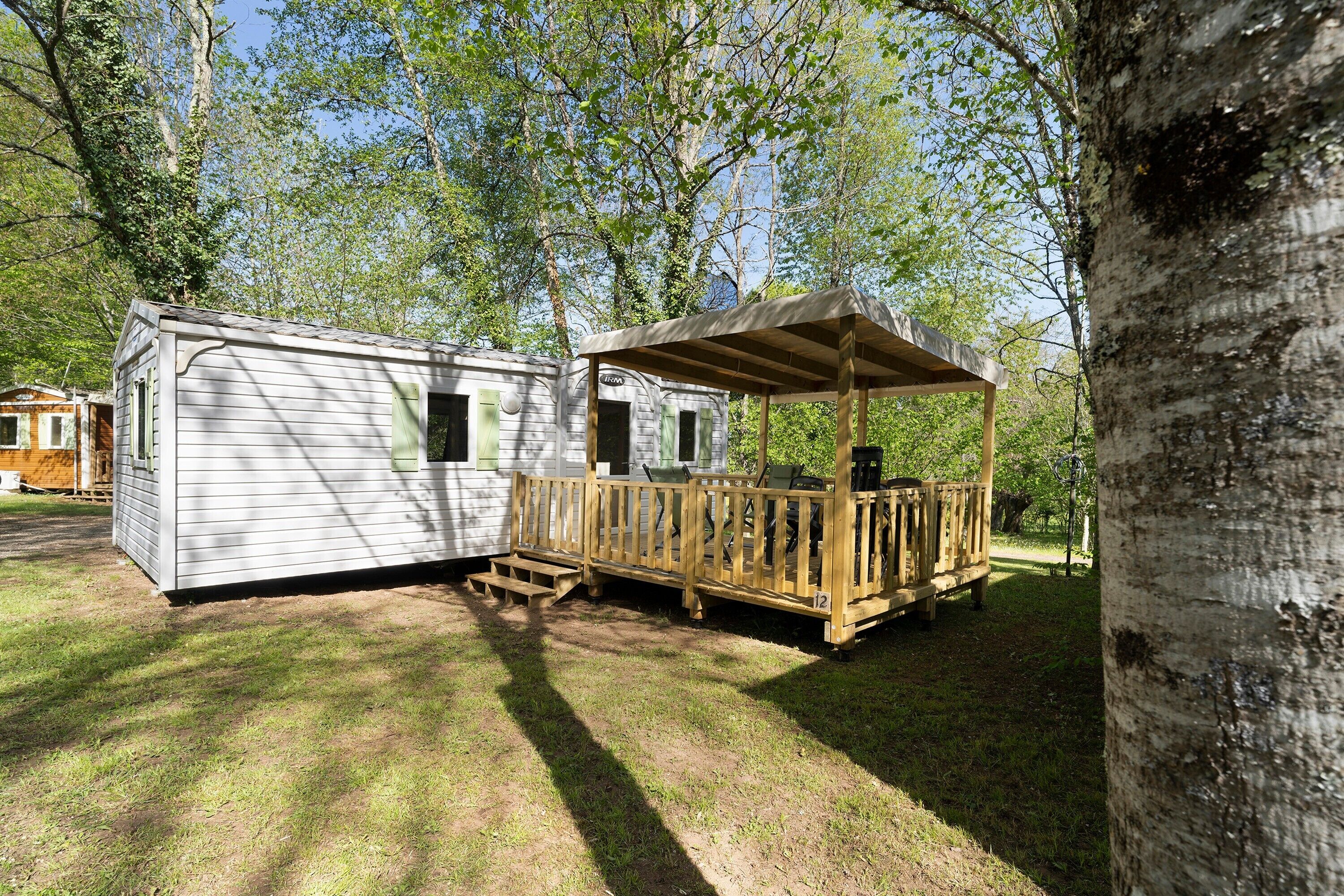 A mobile home with a porch and a covered area, surrounded by trees.